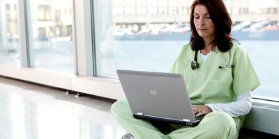 Clinicienne assise sur le sol et regardant son ordinateur portable
